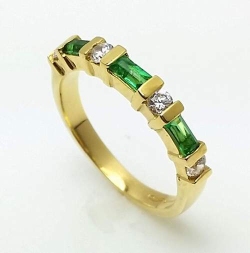 Gold ring with green gemstones and diamonds on a white background